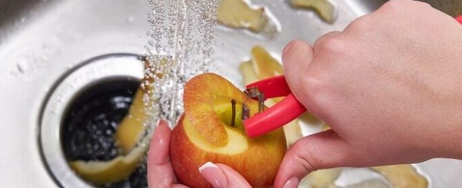 garbage disposal with running water and person peeling apple into kitchen sink